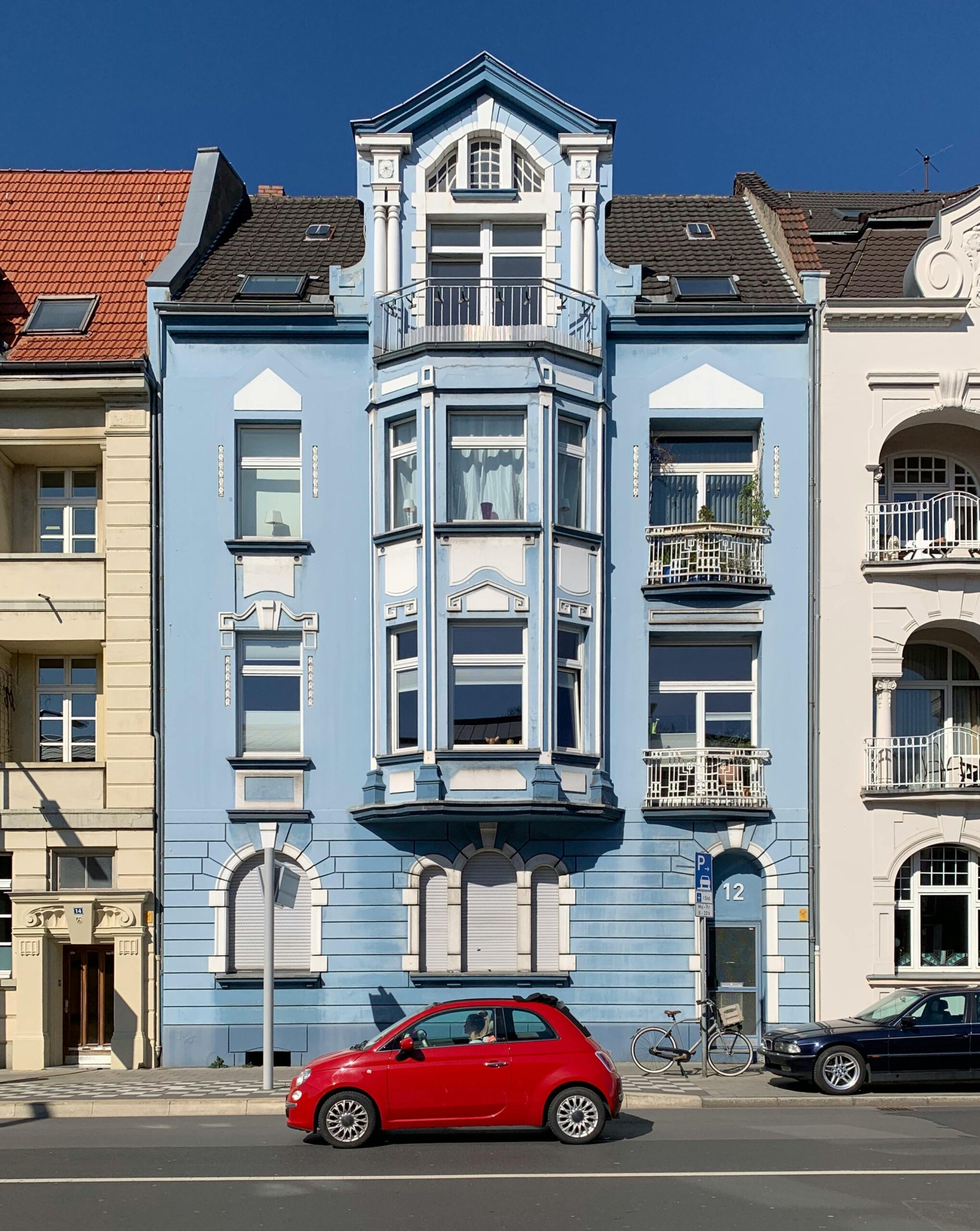 Vibrant blue residential building facade with a red car in Düsseldorf.